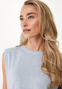 Jasnoniebieski bezrękawnik z okrągłym dekoltem, wykonany z miękkiego materiału. Posiada subtelną teksturę i luźny krój, który podkreśla naturalne włosy.