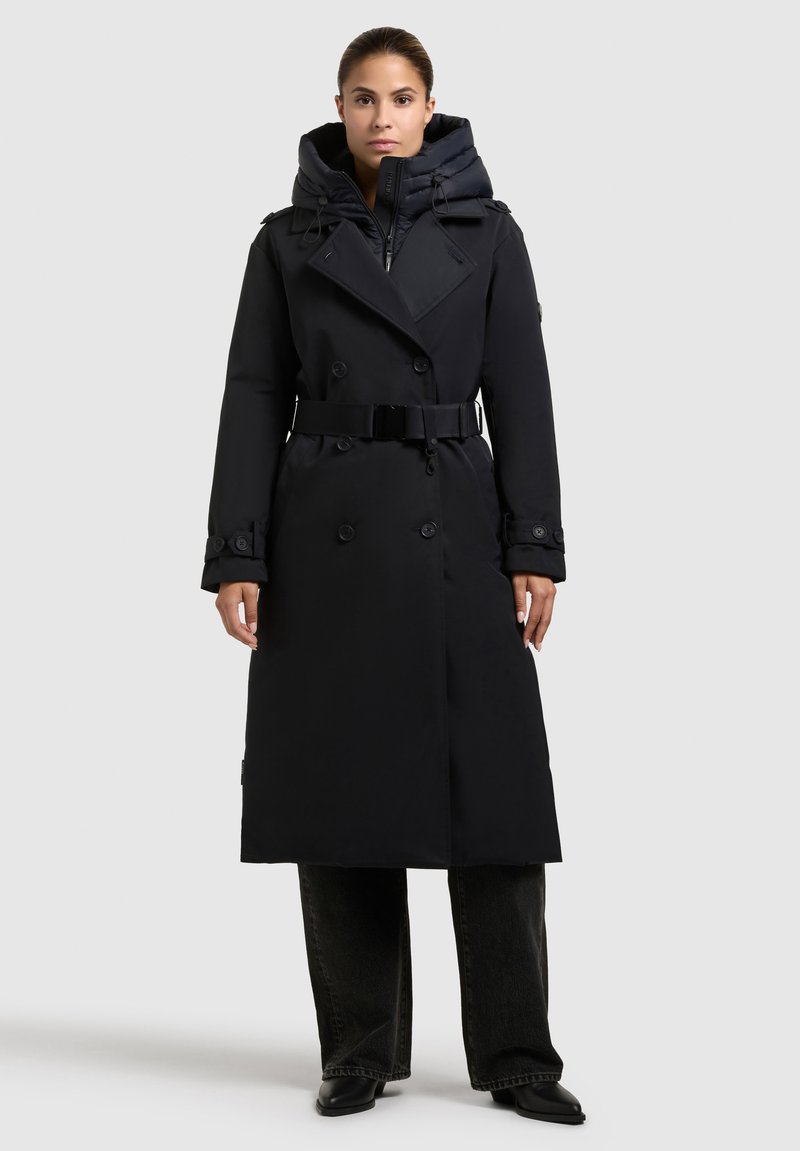 Abrigo negro tipo trench con capucha, diseño de doble botonadura, bolsillos laterales y cintura ajustada con cinturón. Presenta una textura suave y detalles de botones.