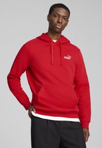 Rød hættetrøje med en kængurulomme, lavet af blødt materiale. Har et hvidt Puma-logo på den øverste venstre side og en snørret hætte.