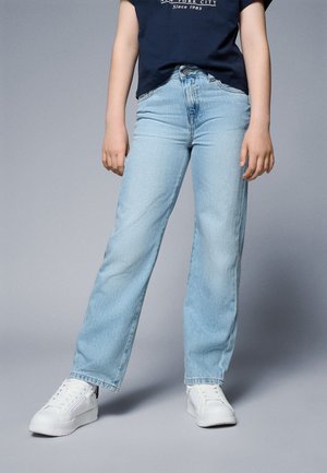Jean droit bleu clair en denim, avec une taille mi-haute, un léger délavage, et un design classique à cinq poches, associé à des baskets blanches.
