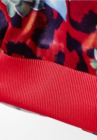 Červená elastická guma na spodní straně s květinovým vzorem v modré, zelené a tmavě červené barvě. Hladká textilie.