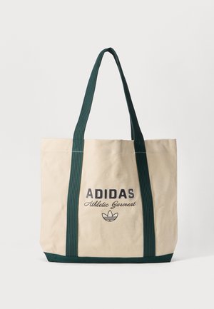Sac tote beige Adidas avec des poignées et un fond vert foncé, affichant le texte et le logo "Adidas Athletic Garment" sur le devant.