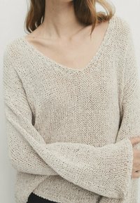 Light beige knitted sweater with a V-neck, loose fit, and long sleeves, featuring a textured pattern and visible stitching details.