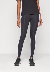 Leggings sportivi neri con strisce bianche ai lati, realizzati in materiale elastico. Abbinati a una t-shirt nera e sneakers nere.