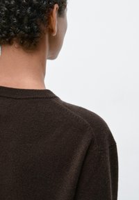 Brązowy sweter dziergany na drutach, z okrągłym dekoltem, miękka faktura, bez widocznych wzorów, widoczny od tyłu z zbliżeniem na ramię i okolice szyi.