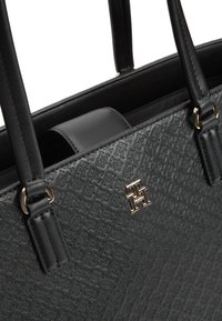 Μαύρη δερμάτινη τσάντα ώμου με ανάγλυφο σχέδιο, χρυσό λογότυπο "TH" και διπλές λαβές με μεταλλικούς κρίκους.