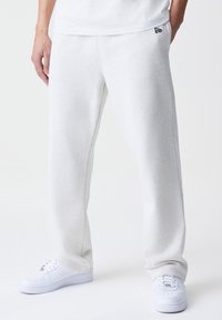 Pantalones de chándal de color gris claro, hechos de una tela suave, con una cintura elástica y bolsillos laterales, combinados con zapatillas blancas.