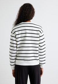 Sudadera blanca con rayas horizontales negras, cuello redondo, puños y dobladillo de canalé. Tejido suave, corte holgado y diseño minimalista sin logotipos.