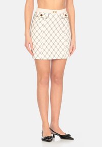 Gonna corta realizzata in tessuto leggero, caratterizzata da un intricato motivo a diamante in nero e beige. Include tasche frontali con dettagli dorati.