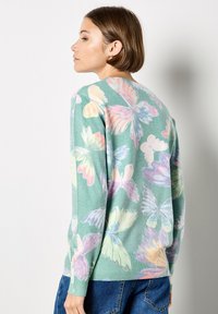 Zielony sweter z motywem motyla w pastelowych kolorach, z okrągłym dekoltem i ściągaczami przy rękawach, wykonany z miękkiego materiału.