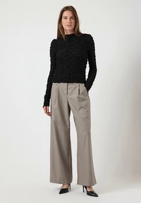 Top nero a maniche lunghe con tessuto testurizzato e collo alto, abbinato a pantaloni beige a gamba larga e décolleté nere con punta appuntita.