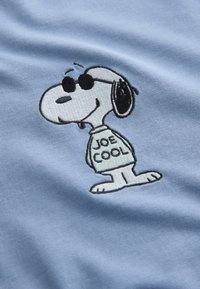 Svetlomodrá tkanina s vyšitým kresleným psom v slnečných okuliaroch a tričku s textom "JOE COOL". Hladká textura, jednoduchý dizajn.
