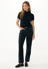 Top negro de manga corta combinado con jeans negros de cintura alta. Textura suave, corte relajado y mocasines negros elegantes completan el atuendo.
