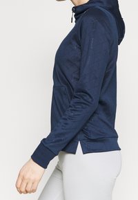 Marinblå zip-up hoodie med ett kviltat diamantmönster, mjukt tyg, framficka och ribbade ärmslut. Har en huva med snörning och sidoverskärningar.