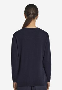 Granatowy sweter z długim rękawem o okrągłym dekolcie. Miękka, gładka tekstura oraz ściągacze przy mankietach i u dołu. Brak widocznych wzorów lub detali z metalu.