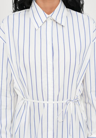 Camicia bianca con bottoni, caratterizzata da righe verticali blu, collo e cintura in vita. Realizzata in tessuto morbido con maniche lunghe.