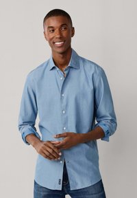 Camicia azzurro chiaro in cotone con colletto a punta, maniche lunghe e bottoni bianchi. Presenta una piccola etichetta del marchio sull'orlo.