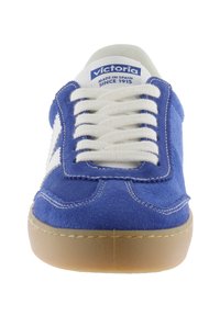 Baskets en daim bleu avec lacets blancs, logo blanc et semelle en caoutchouc. Présente des détails cousus. Vue de face mettant en valeur la forme et le design.