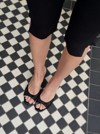 Čierne sandále na otvorenej špičke majú textúrovaný dizajn a mašľový detail vpredu. Podrážky sú ploché a materiál vyzerá hladko a flexibilne.
