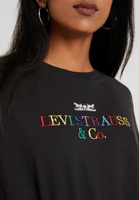 Černé bavlněné tričko s vícebarevným vyšívaným textem "LEVI STRAUSS & Co." a logem nahoře. Kulatý výstřih a volný střih.