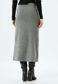 Jupe midi en tricot côtelé gris avec une taille cintrée, associée à des bottes noires à talons hauts montantes. Texture lisse, design minimaliste.