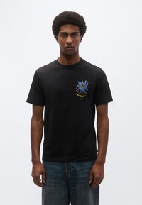 Μαύρο βαμβακερό κοντομάνικο μπλουζάκι με σχέδιο σε μπλε και πορτοκαλί χρώμα που απεικονίζει ένα λουλούδι και κείμενο στην αριστερή πλευρά του στήθους.