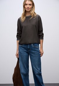 Top nero in seta a maniche lunghe con orlo elastico e polsini a righe, abbinato a jeans in denim blu a gamba larga e una borsa in suede marrone.