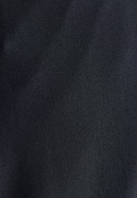 Zbliżenie ciemnoszarej tkaniny o drobnej, tkanej fakturze, na której widoczne są małe, równomiernie rozmieszczone nici.