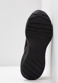 Black rubber shoe sole with textured tread patterns and branded lettering. Size marked as 37, angled against a light background.