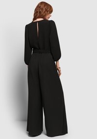 Combinaison noire à coupe décontractée, avec de longues manches bouffantes et un détail dos en trou de serrure. Fabriquée en tissu doux avec une taille ceinturée.