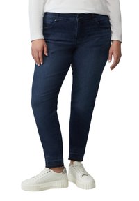 Dunkelblaue Jeans mit slim Fit, aus Jeansstoff, mit fünf Taschen und einem Knopfverschluss, kombiniert mit weißen Sneakers.