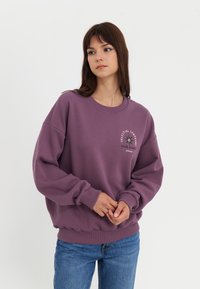 Paarse crewneck sweatshirt met een grafische print met de tekst "Celestial Symphony Solar Eclipse." Ruime pasvorm met geribde boorden en onderkant.