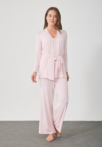 Σετ lounge σε ανοιχτό ροζ χρώμα που περιλαμβάνει ένα μακρυμάνικο σετ τύπου wrap με ζωνάκι και μακριά παντελόνια με φαρδιά πόδια, φτιαγμένο από απαλό και λείο ύφασμα.