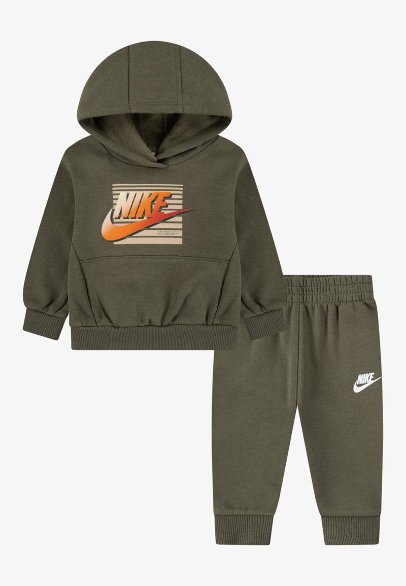 Maslinasto zeleni Nike trenerka koja uključuje duksericu s kapuljačom i logom, s prugama, u kombinaciji s odgovarajućim hlačama s elastičnim pojasom. Mekani materijal.