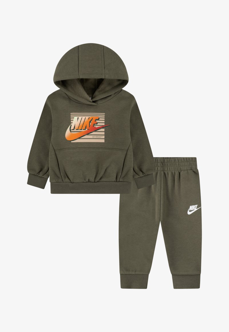 Olivnozelen trenirka Nike, ki vključuje kapuco s sweatshirtom z logotipom in črtami, v kombinaciji z ustreznimi hlačami z elastičnim pasom. Mehka tkanina.