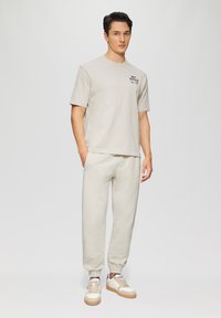 Beige katoenen t-shirt met korte mouwen, voorzien van een klein gedrukt logo. Gecombineerd met bijpassende beige joggers en lichtgekleurde sneakers.
