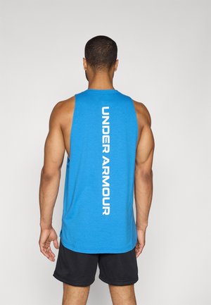 Man draagt een blauw mouwloos Under Armour shirt met wit verticaal logo en zwarte sportshorts, staand met zijn rug naar ons toe op een effen achtergrond.