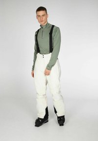Lichtgroene langesleeve zip-top, witte skibroek met bretels en zwarte skischoenen. Glad materiaal met een aansluitend ontwerp en contrasterende kleuren.