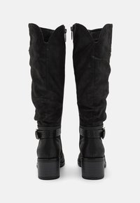 Bottes noires montant jusqu'au genou en daim doux, avec un haut festonné, une bride décorative à boucle et un talon bloc.