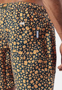 Men's swim shorts in a navy blue fabric featuring an all-over pattern of small yellow elephants. Elastic waistband with a back pocket.