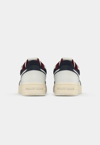 Ténis brancos e azuis marinhos com detalhes em vermelho, apresentando um cabedal em pele texturada, colarinho acolchoado e sola em borracha estampada com "TOMMY JEANS."