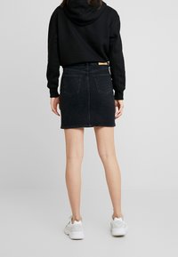 Jupe en denim noir avec une coupe droite, dotée de deux poches arrière et d'une finition épurée. Associée à un hoodie noir et des baskets blanches.