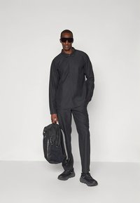 Conjunto de tecido preto com camisa de colarinho e calças, combinado com uma mochila escura e ténis pretos; textura suave e design minimalista.