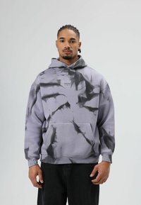 Grijs-paarse hoodie met zwart tie-dye patroon, grote voorkantzak en verstelbare trekkoord capuchon. Gemaakt van katoen, met een losse pasvorm.