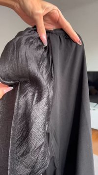 Sort beklædning med en blanding af strukturerede og glatte stoffer. Den ene side har en krøllet tekstur, mens den anden er flad. Elastisk talje.