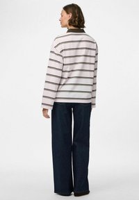 Heledad pikad varrukad särk heleses roosas toonides tumepruuni kaelusega; omab horisontaalseid jooni ja laia lõiget, kombineeritud tumedate laia säärtega teksadega.