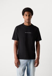 Black cotton t-shirt with a round neckline and short sleeves. Features a white logo text "SCOTCH & SODA" centered on the chest.