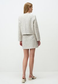 Completo in tweed a due pezzi, composto da una giacca corta e una mini gonna, prevalentemente crema con strisce blu e gialle. Scarpe con tacco a blocco, facili da indossare.