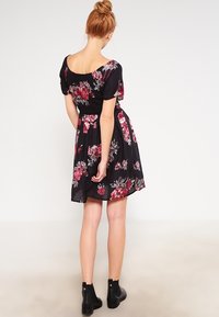 Robe florale noire à manches courtes, avec un corsage ajusté et une jupe évasée. Le motif comprend des roses rouges et roses sur un fond sombre.