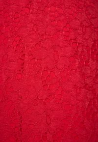 Tissu en dentelle rouge avec des motifs floraux et des détails ajourés créant une surface texturée et décorative.